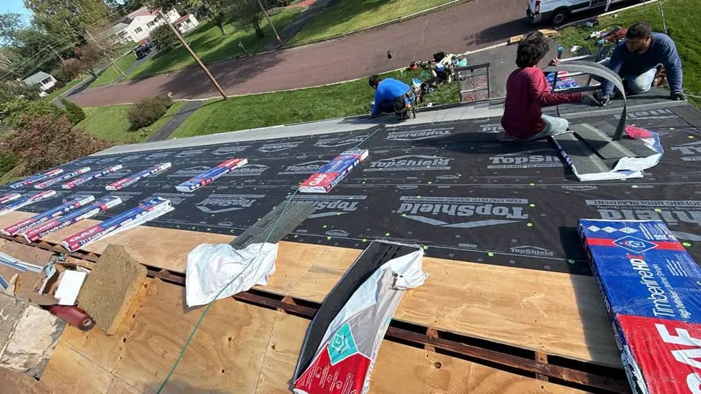 Crew laying underlayment beside exposed plywood on the Chalfont roof
