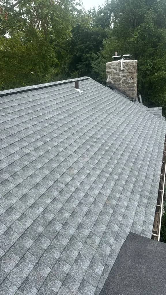 Completed gray shingle roof planes beside a stone chimney in Penn Wynne