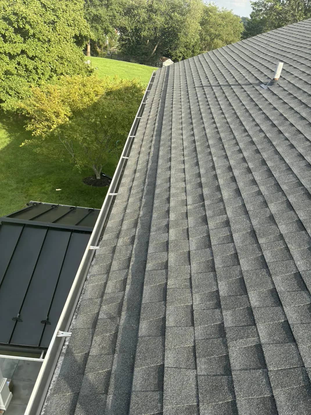 Finished shingle slope beside the gutter with a pipe vent near the upper roof